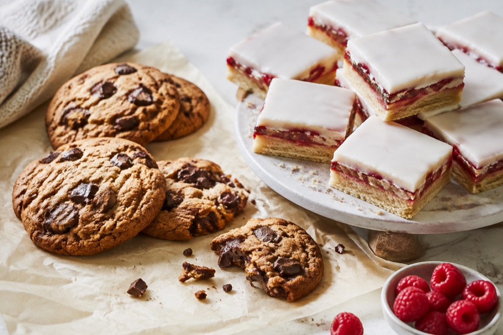 Chokoladecookies og glaserede hindbærsnitter på et lyst bord